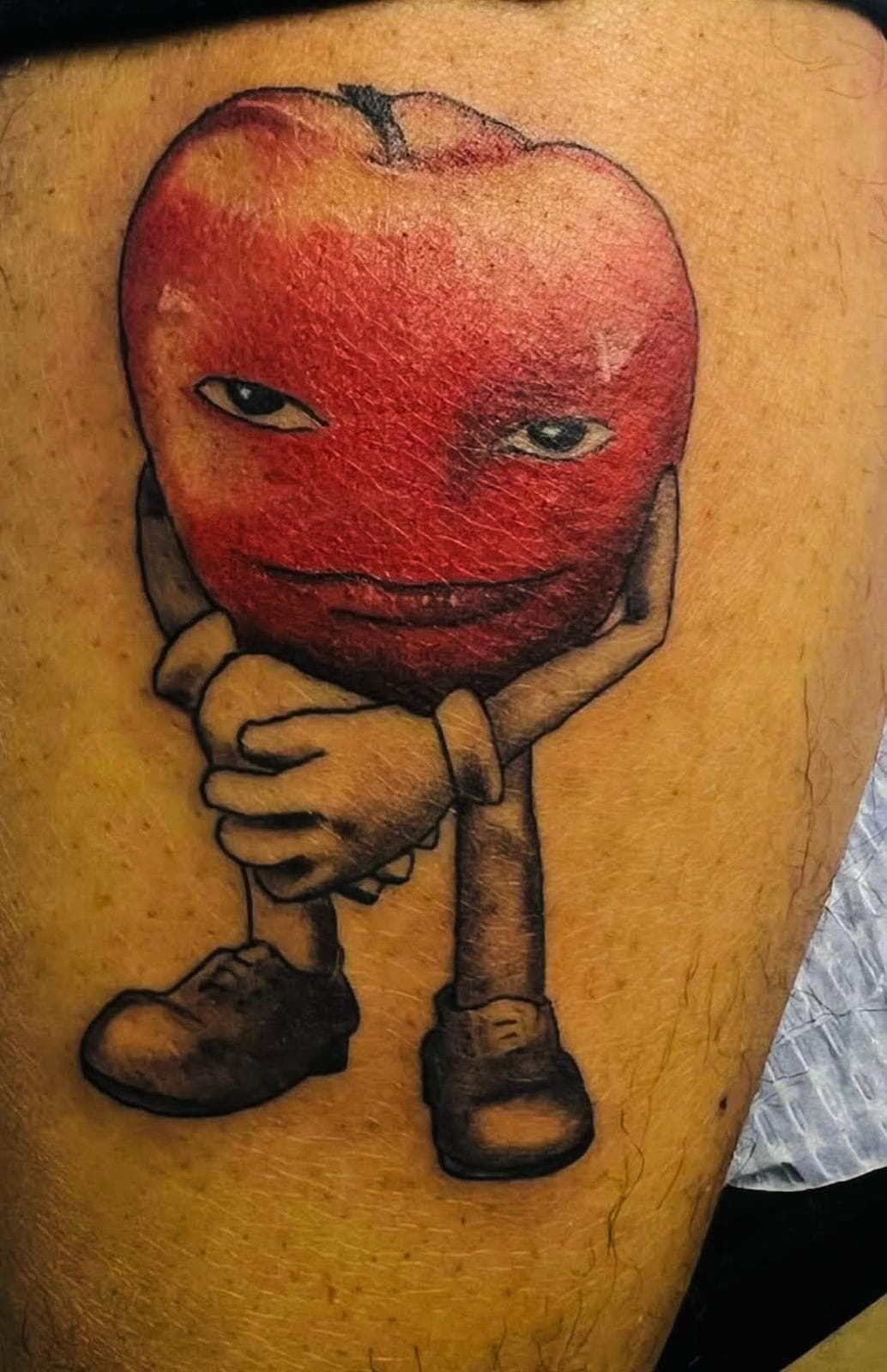 Illustrative red apple character tattoo on upper arm by Alison at Inked City Tattoos in Trenton, NJ